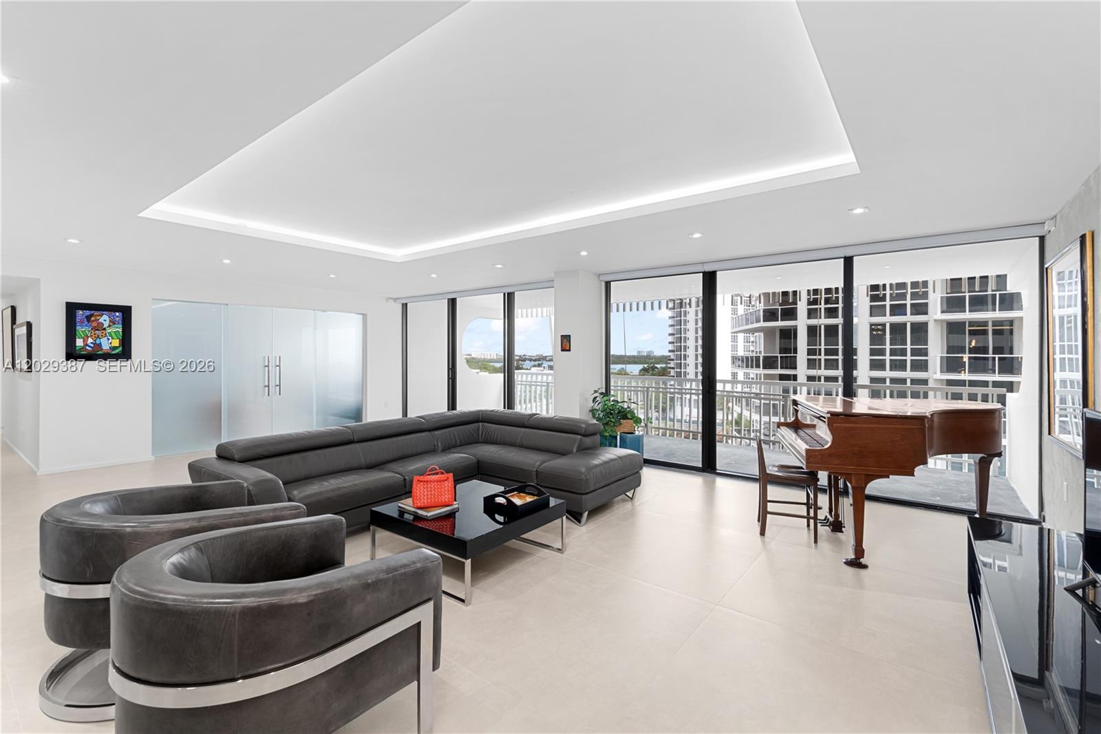 A modern living room features a large gray sectional, two armchairs, a grand piano, and floor-to-ceiling windows — 10205 Collins Ave # 604, Bal Harbour FL 33154, BAL HARBOUR, FL