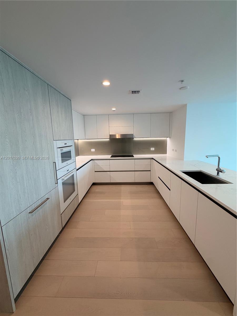A modern kitchen features white cabinetry, light wood flooring, and a stainless steel oven stack — 9221 E Bay Harbor Dr # 309, Bay Harbor Islands FL 33154, BAY HARBOR ISLANDS, FL