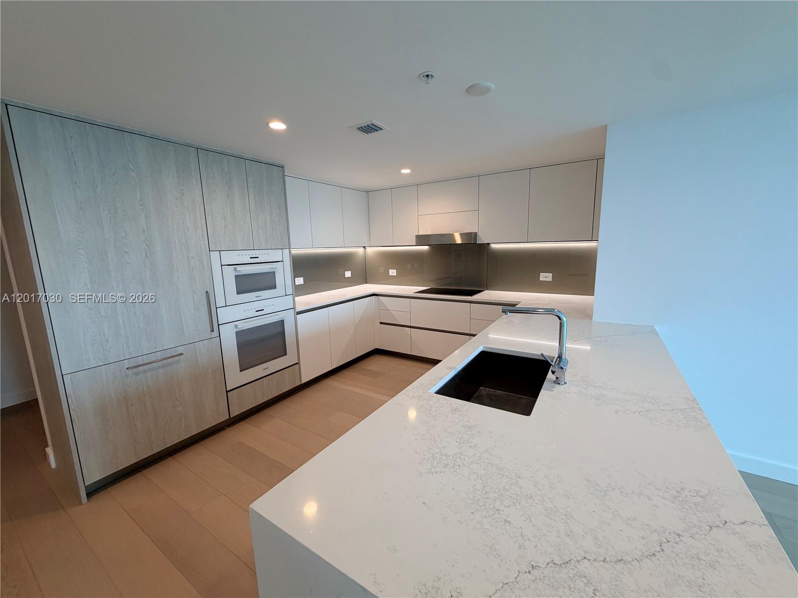 A modern kitchen features light wood cabinetry, white countertops, a kitchen island, and stainless appliances — 9221 E Bay Harbor Dr # 309, Bay Harbor Islands FL 33154, BAY HARBOR ISLANDS, FL