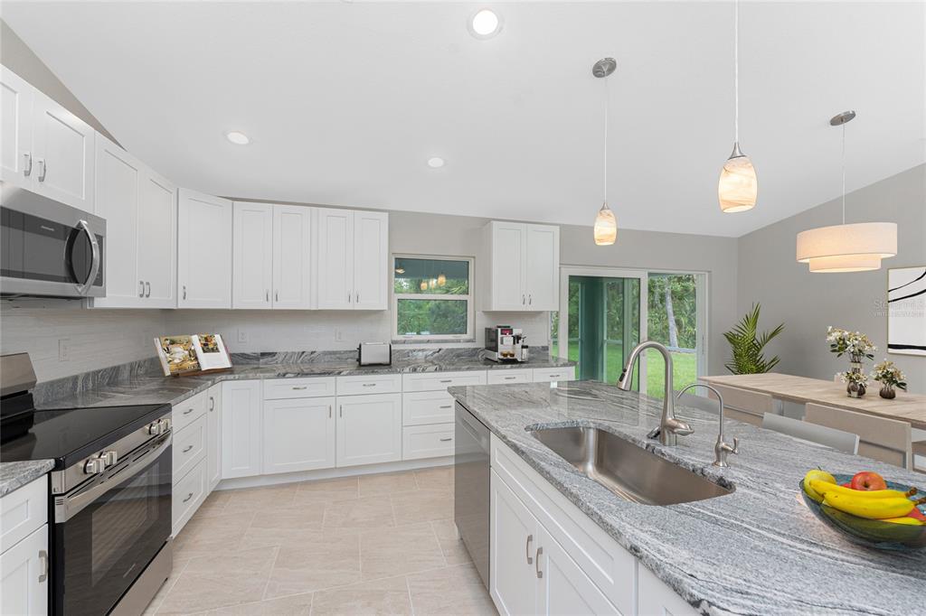 A modern kitchen features white cabinets, granite countertops, a large island, and stainless steel appliances — 1425 LINDSAY AVENUE, NORTH PORT, FL