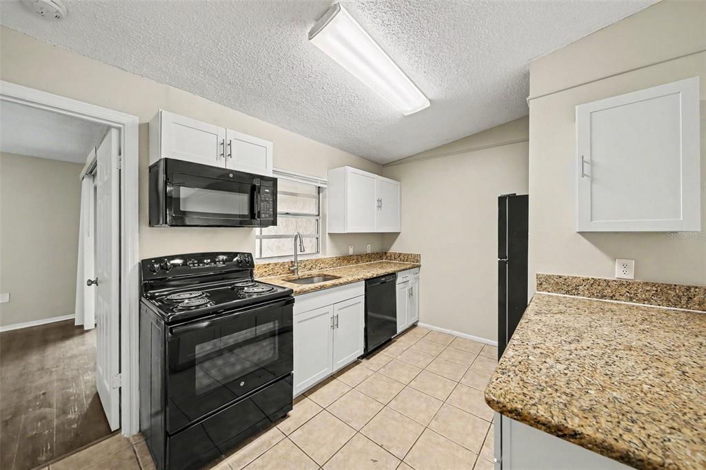 A kitchen features white cabinets, black appliances, granite countertops, and light tile flooring — 1188 WOODMAN WAY, ORLANDO, FL