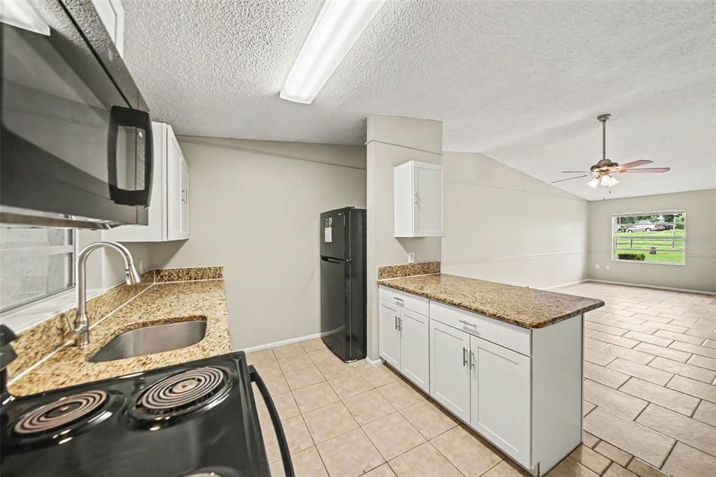 A kitchen with white cabinets, granite countertops, and black appliances opens to a living area — 1188 WOODMAN WAY, ORLANDO, FL