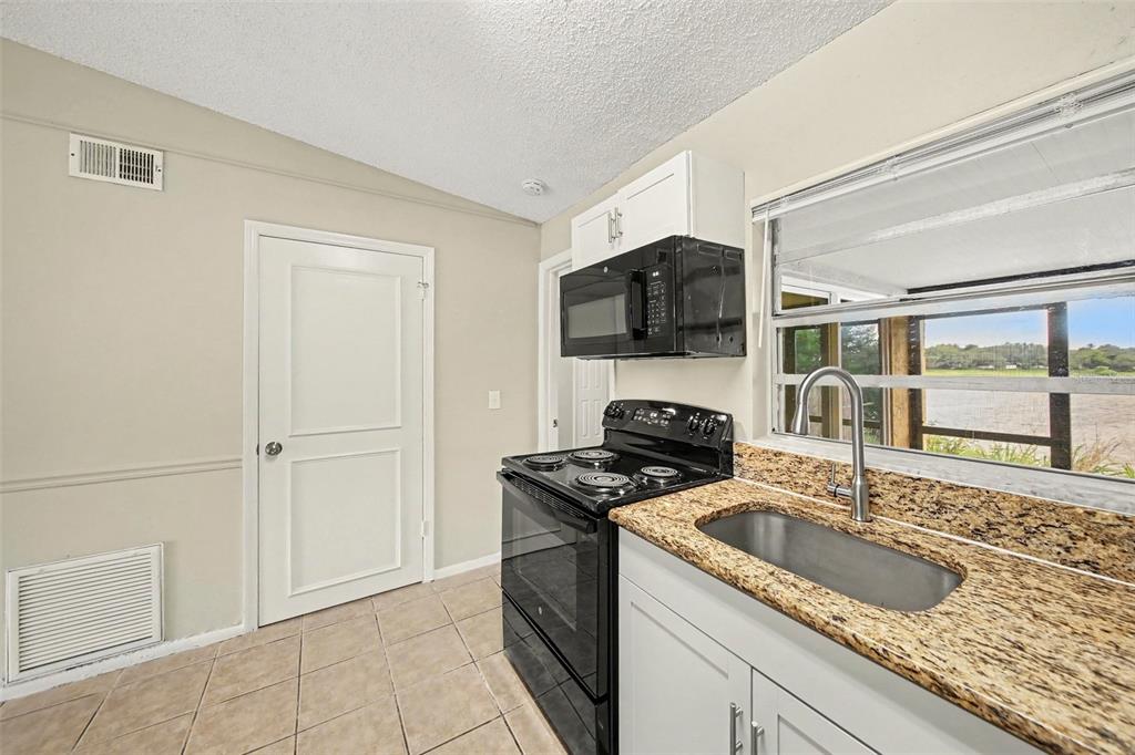 A kitchen features a black stove, microwave, granite countertops, and a sink by a window — 1188 WOODMAN WAY, ORLANDO, FL