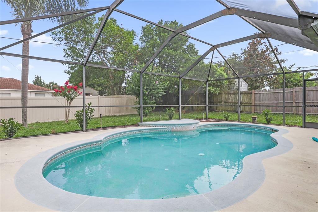 A swimming pool with a raised spa is enclosed by a screened lanai in a backyard — 1762 HOWLAND BOULEVARD, DELTONA, FL