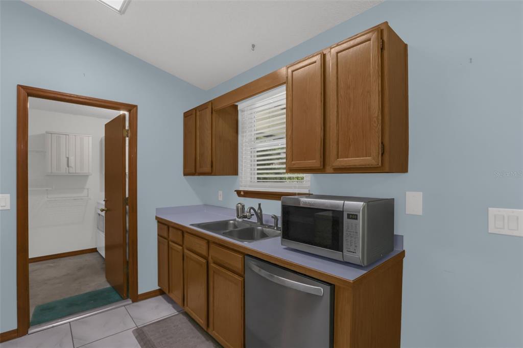 A kitchen features light blue walls, wood cabinets, a stainless steel microwave, and a dishwasher — 1762 HOWLAND BOULEVARD, DELTONA, FL