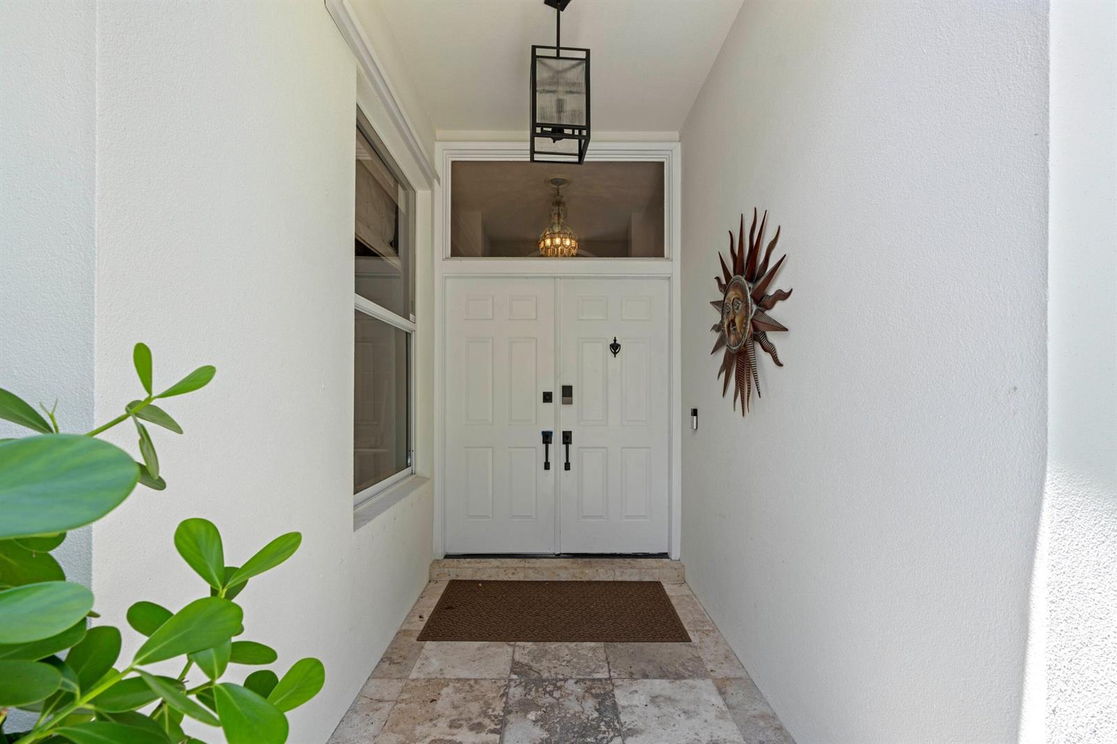 A white double door entrance features a transom window, a sun wall hanging, and tile — 1205 Gator Trail, West Palm Beach FL 33409, WEST PALM BEACH, FL