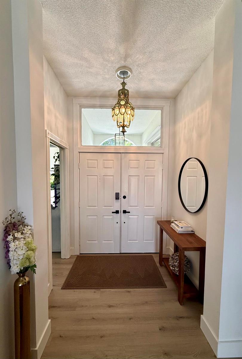 An entryway features a double door, a chandelier, a console table, and a round mirror — 1205 Gator Trail, West Palm Beach FL 33409, WEST PALM BEACH, FL