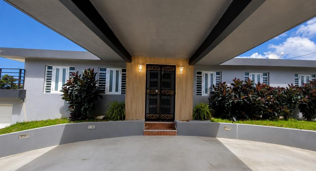 A gray house exterior features a covered driveway, a central entryway, and large green shrubs — 30 SAN AGUSTIN, SAN JUAN, PR