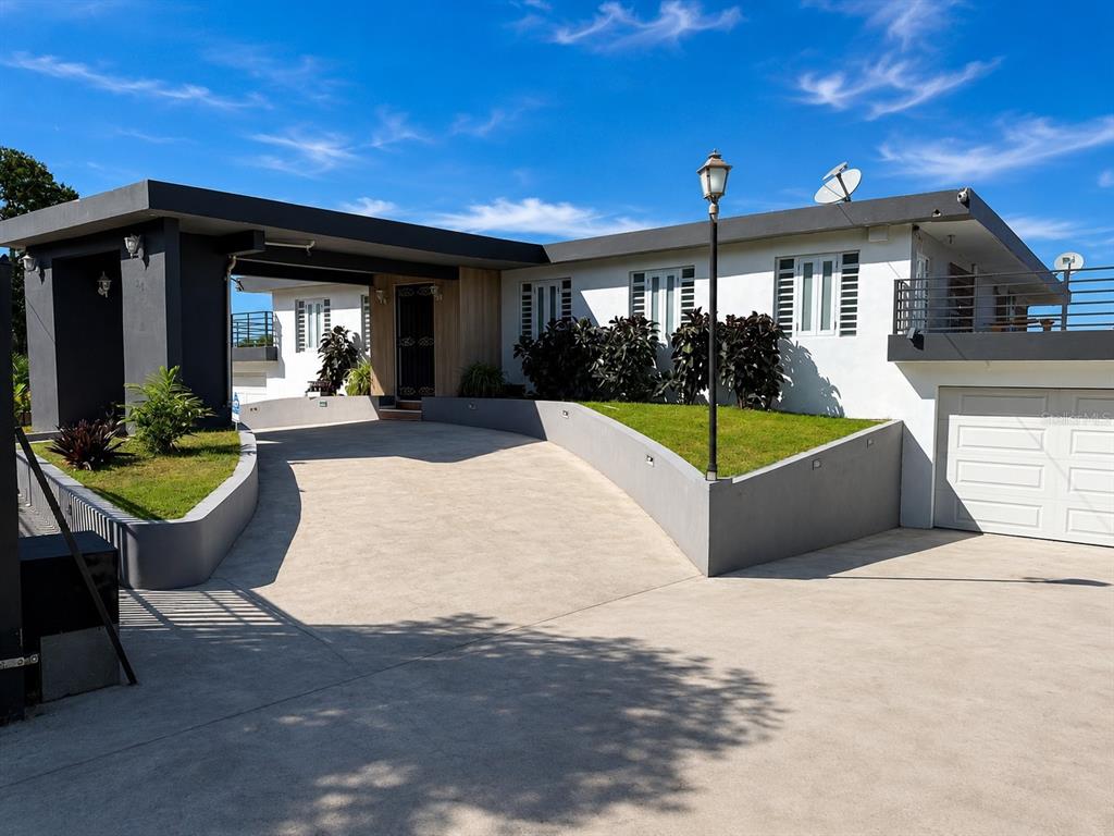 A modern one-story house with a concrete driveway, carport, and elevated lawn area — 30 SAN AGUSTIN, SAN JUAN, PR
