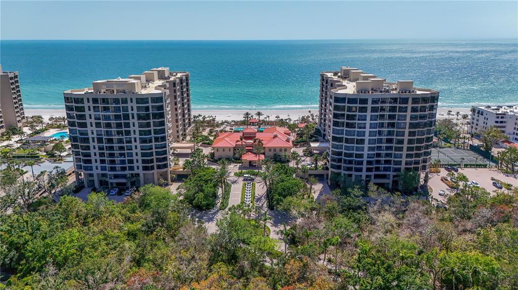 An aerial view shows two high-rise residential buildings flanking a clubhouse near a sandy beach — 1241 GULF OF MEXICO DRIVE UNIT 603, LONGBOAT KEY, FL