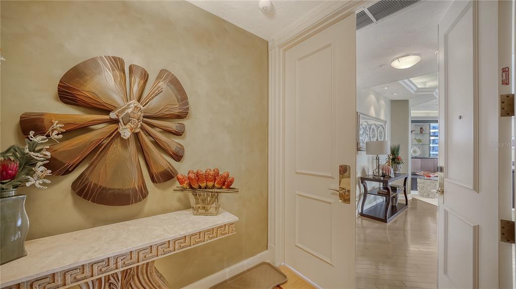 An entryway features a beige wall with a large metal flower sculpture and console table — 1241 GULF OF MEXICO DRIVE UNIT 603, LONGBOAT KEY, FL