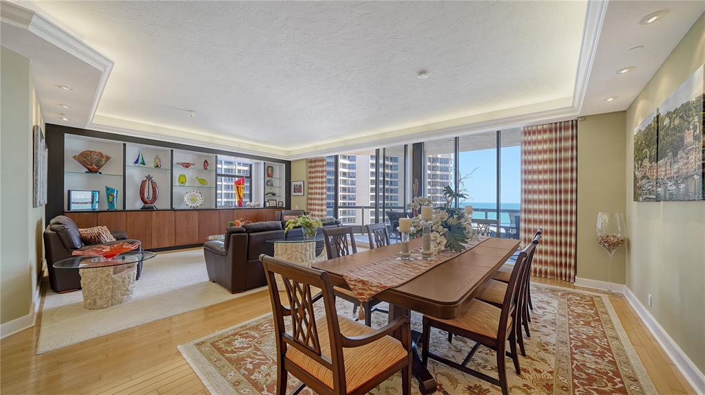 A dining area and living room with hardwood floors, a large built-in shelf, and ocean views — 1241 GULF OF MEXICO DRIVE UNIT 603, LONGBOAT KEY, FL
