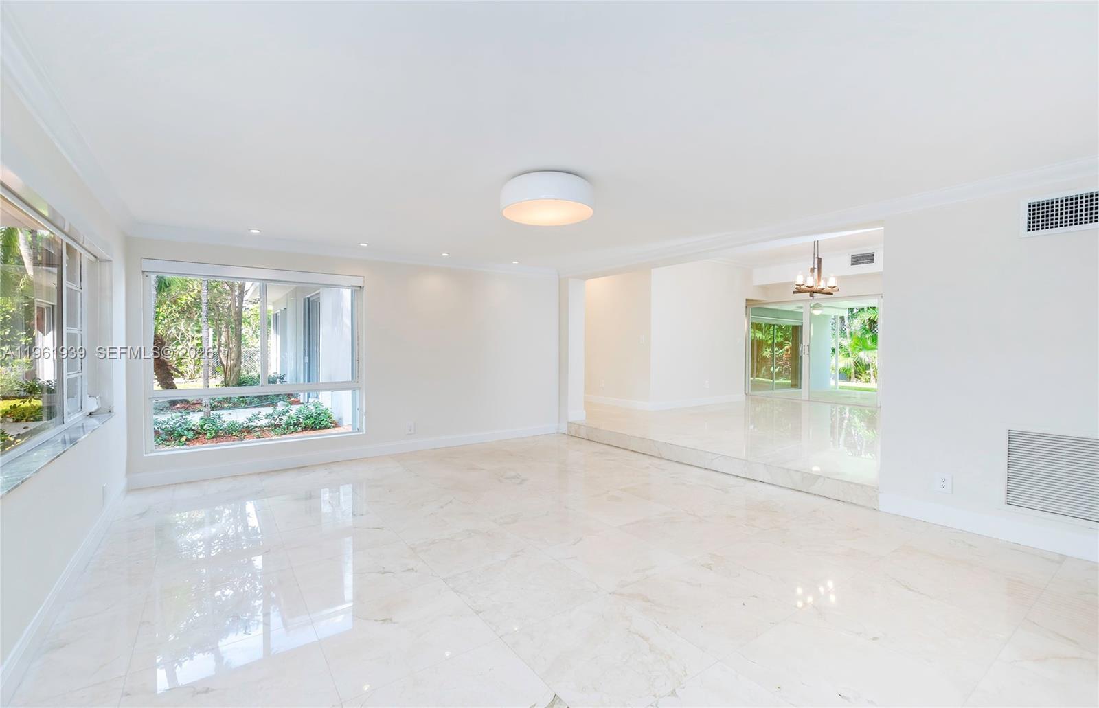 A bright, empty living room features white walls, marble tile flooring, and large windows — 310 Harbor Ct, Key Biscayne FL 33149, KEY BISCAYNE, FL
