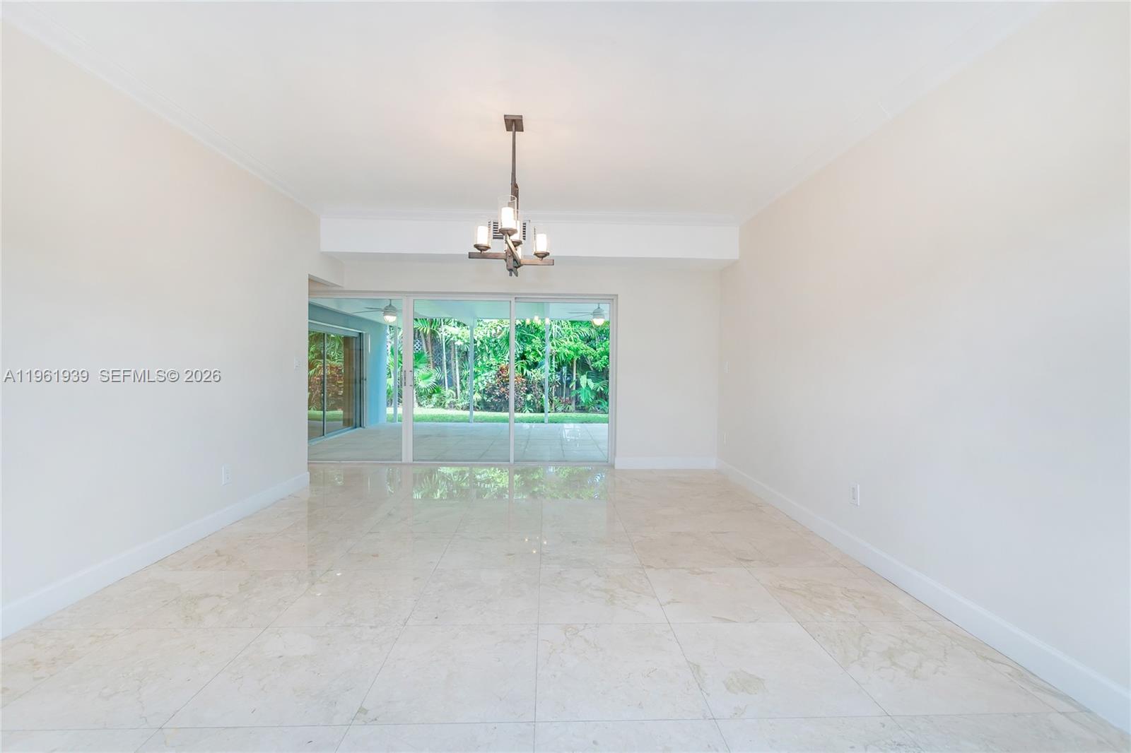 An empty dining room features light-colored tile flooring, a modern chandelier, and sliding glass doors — 310 Harbor Ct, Key Biscayne FL 33149, KEY BISCAYNE, FL
