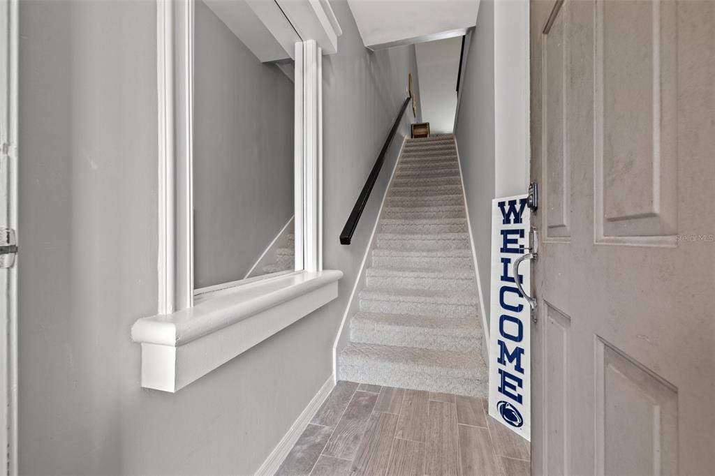 An entryway features a staircase with carpeted steps, gray walls, and wood-look tile flooring — 1039 NORMANDY TRACE ROAD UNIT 1039, TAMPA, FL