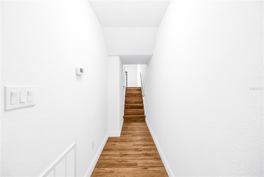 A narrow hallway with white walls and wood-look flooring leads to a set of stairs — 6462 92ND PLACE N UNIT 803, PINELLAS PARK, FL