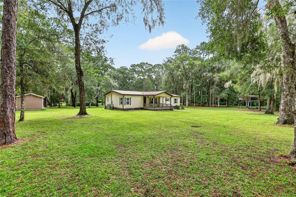 A single-story house with a porch sits on a large, grassy lot with many trees — 7727 CR 659, BUSHNELL, FL