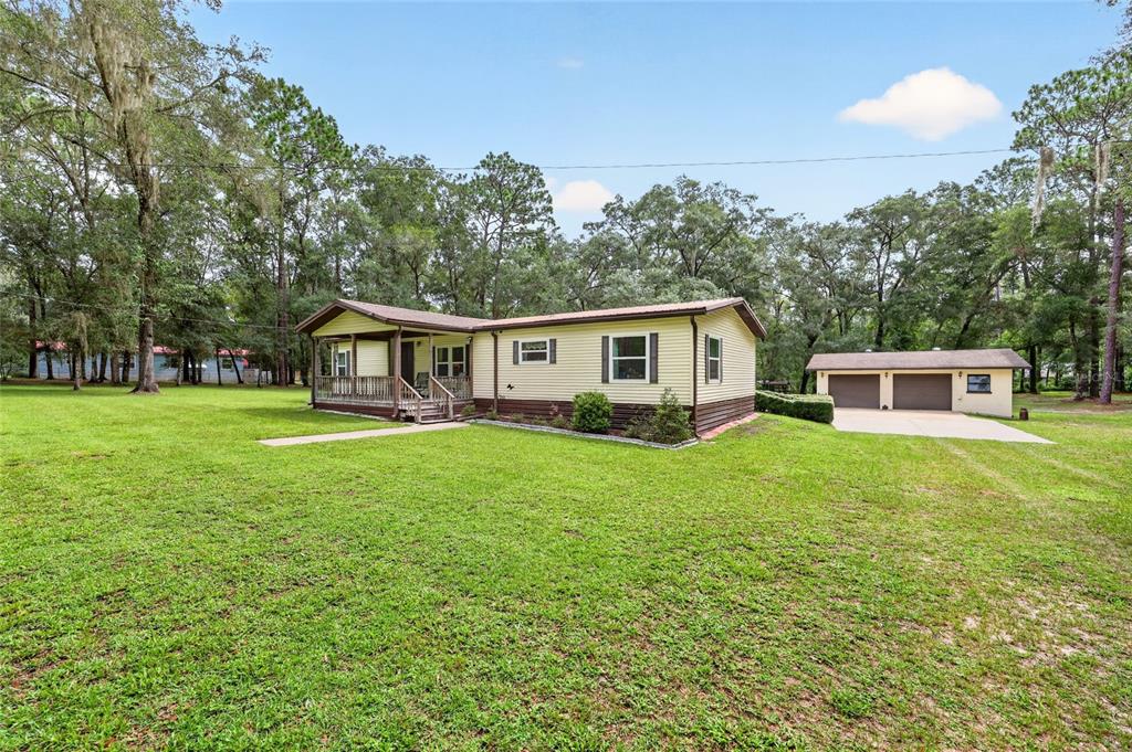 A single-story house with a front porch and a detached two-car garage on a lawn — 7727 CR 659, BUSHNELL, FL