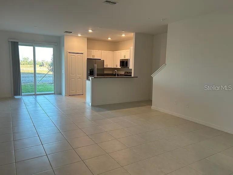 This open-concept living area features tile flooring, a kitchen with white cabinets, and sliding glass doors — 11324 65TH TERRACE E, PALMETTO, FL