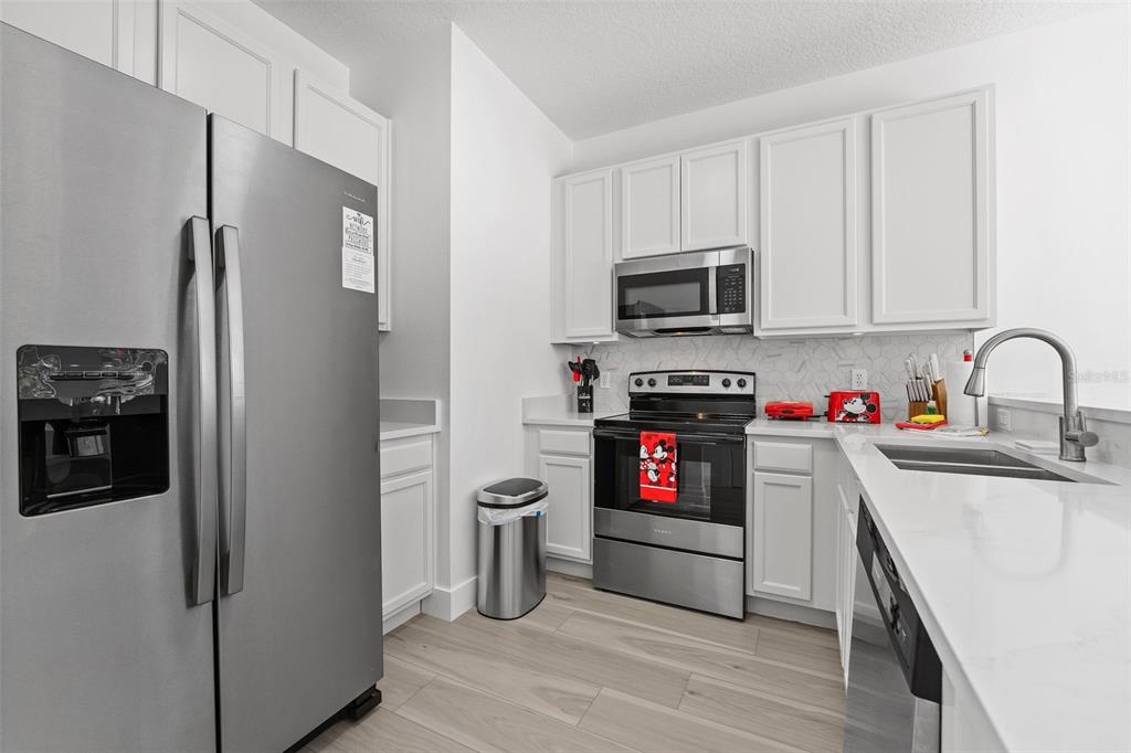A kitchen with white cabinets, stainless steel appliances, light wood-look flooring, and white countertops — 3045 YELLOW LANTANA LANE, KISSIMMEE, FL