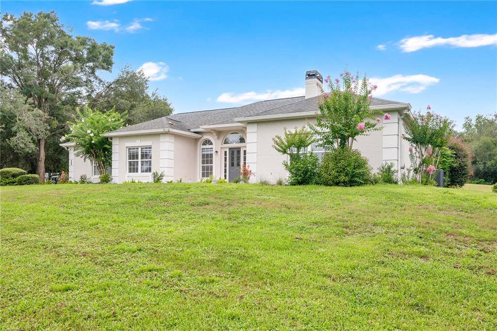 A single-story house with a light-colored stucco exterior sits on a large, grassy lawn — 22841 STALLION DRIVE, SORRENTO, FL