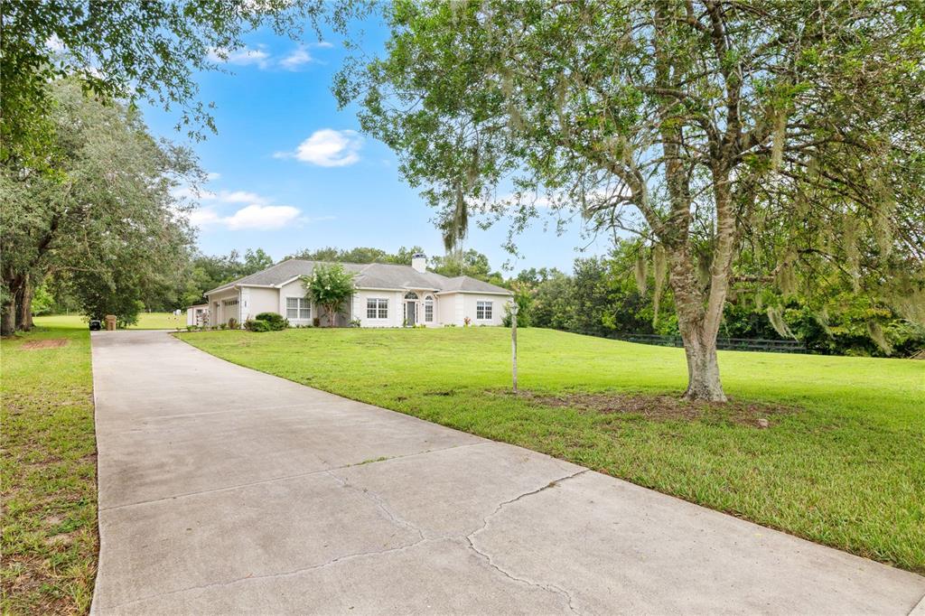 A long concrete driveway leads to a single-story house surrounded by a large grassy lawn — 22841 STALLION DRIVE, SORRENTO, FL