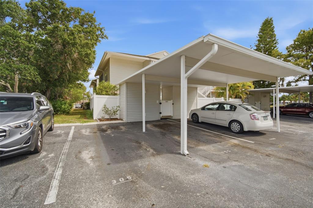 A covered carport with two parking spaces sits in front of a multi-story residential building — 8350 SAVANNAH TRACE CIRCLE UNIT 305, TAMPA, FL