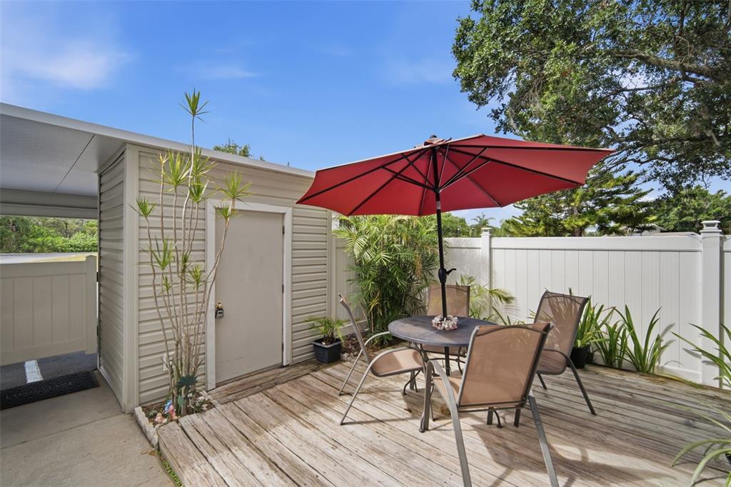 A wooden deck features a patio table with a red umbrella and chairs near a shed — 8350 SAVANNAH TRACE CIRCLE UNIT 305, TAMPA, FL