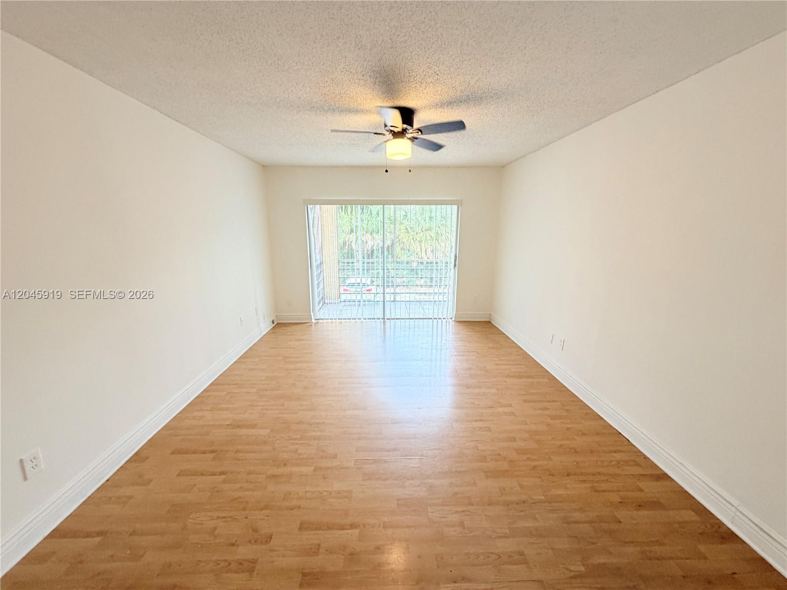 An empty room with light wood-look flooring, white walls, a ceiling fan, and sliding glass doors — 2800 NW 56th Ave # E201, Lauderhill FL 33313, LAUDERHILL, FL