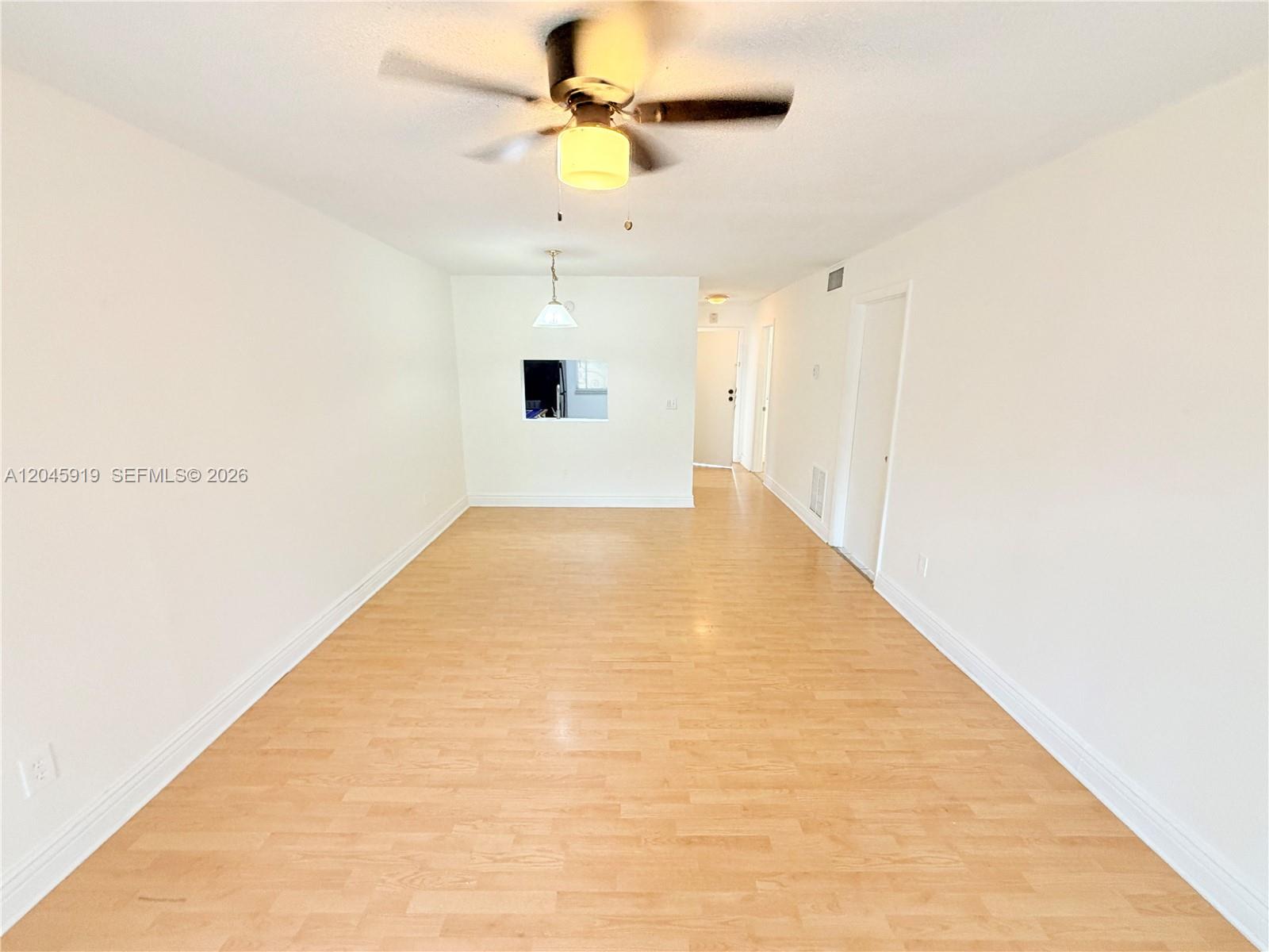 An empty room features light wood-look flooring, white walls, a ceiling fan, and a pass-through — 2800 NW 56th Ave # E201, Lauderhill FL 33313, LAUDERHILL, FL