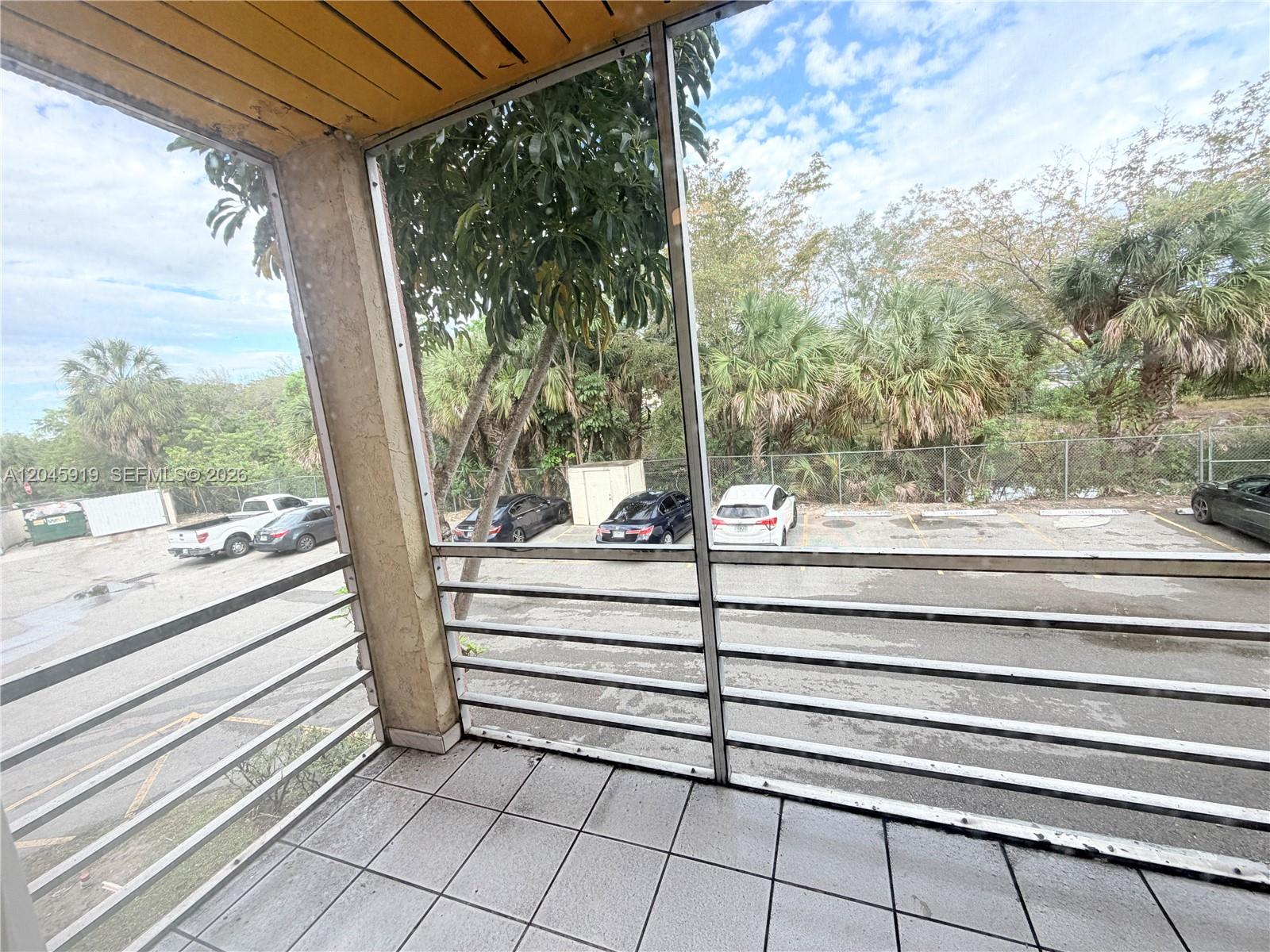 A screened-in balcony with tiled flooring overlooks a parking lot and surrounding trees — 2800 NW 56th Ave # E201, Lauderhill FL 33313, LAUDERHILL, FL