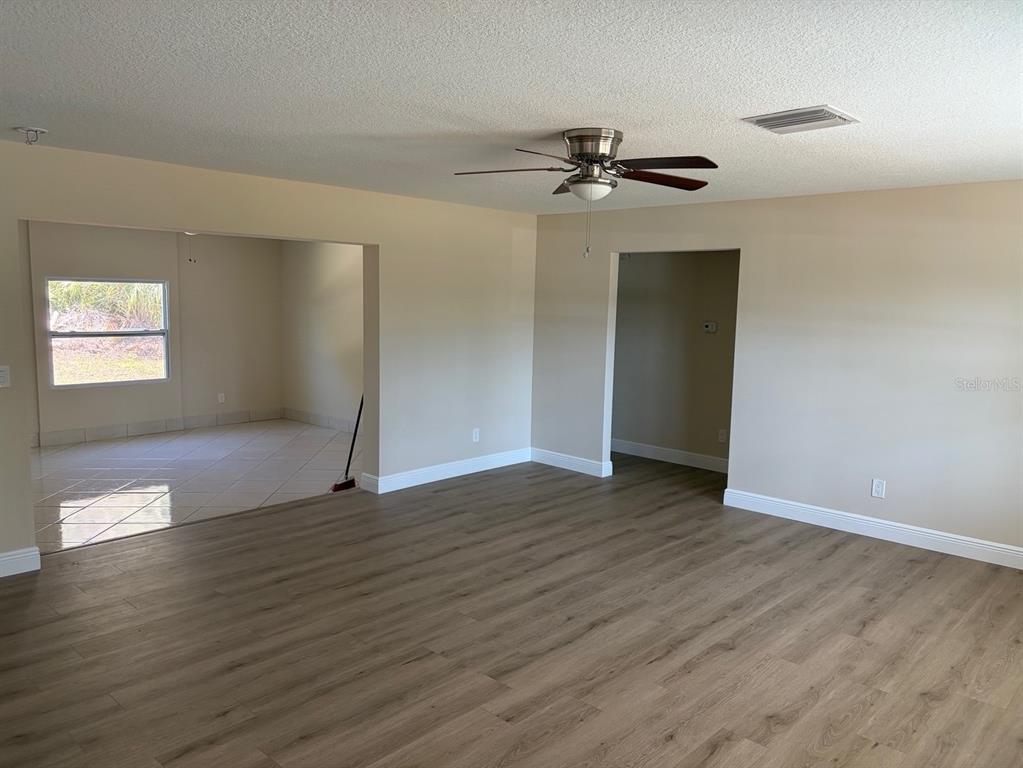 A living room with wood-look flooring, a ceiling fan, and an adjacent tiled room — 201 PALMETTO ROAD, NOKOMIS, FL