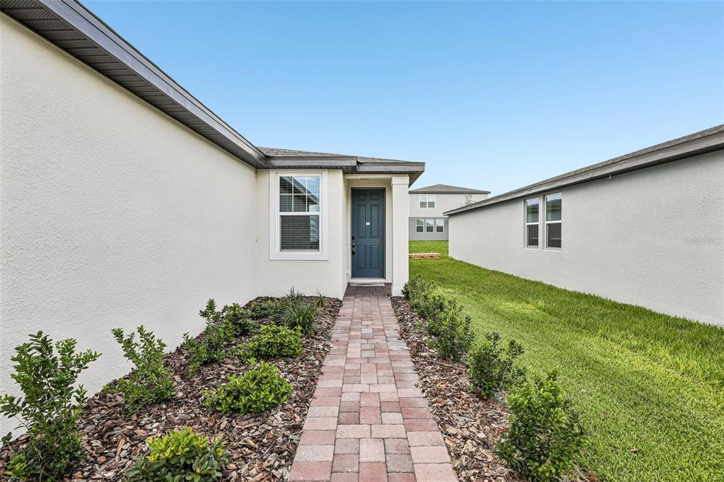A paved walkway leads to the front entrance of a house with light-colored stucco walls — 3713 QUEENSLAND COURT, HAINES CITY, FL