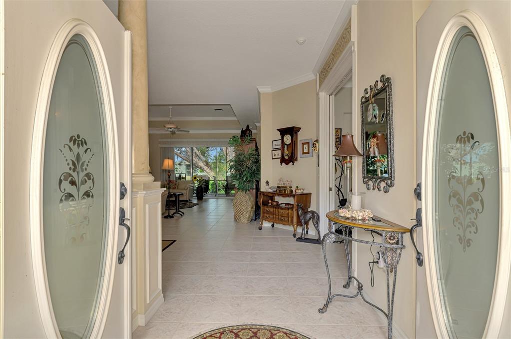 A view from an entryway looking through a tiled hallway toward a living room — 625 MISTY PINE DRIVE, VENICE, FL