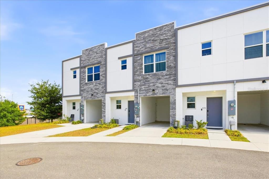 A row of modern townhomes features white siding, stone accents, and integrated ground-level carports — 620 TRIKOMO DRIVE, DAVENPORT, FL