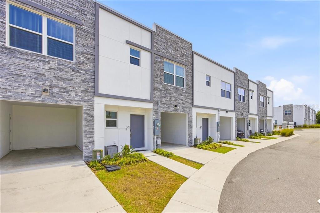 A row of modern townhomes features stone veneer facades, white panels, and integrated ground-level carports — 620 TRIKOMO DRIVE, DAVENPORT, FL