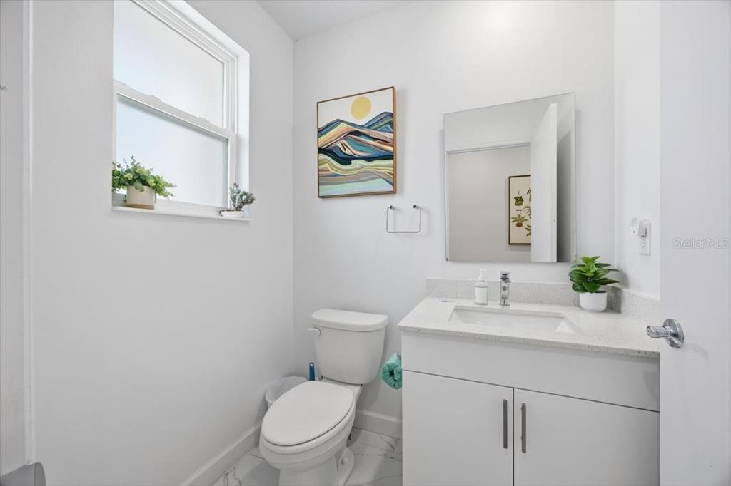 A bright bathroom features a white vanity, a toilet, a window, and abstract wall art — 620 TRIKOMO DRIVE, DAVENPORT, FL