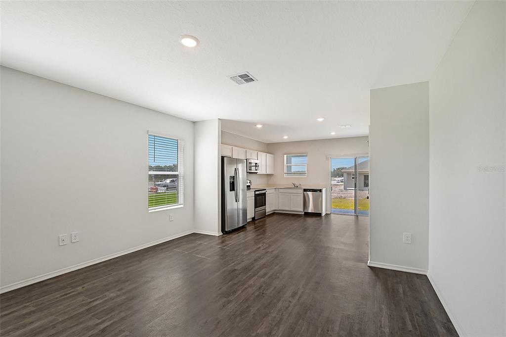 An open-concept kitchen and living area features dark wood-look flooring and stainless steel appliances — 13004 SASSAFRAS TRAIL, PARRISH, FL