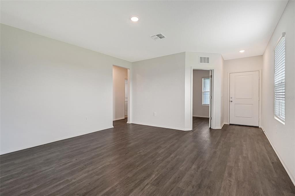 An empty room features light gray walls, dark wood-look flooring, and two interior doorways — 13004 SASSAFRAS TRAIL, PARRISH, FL