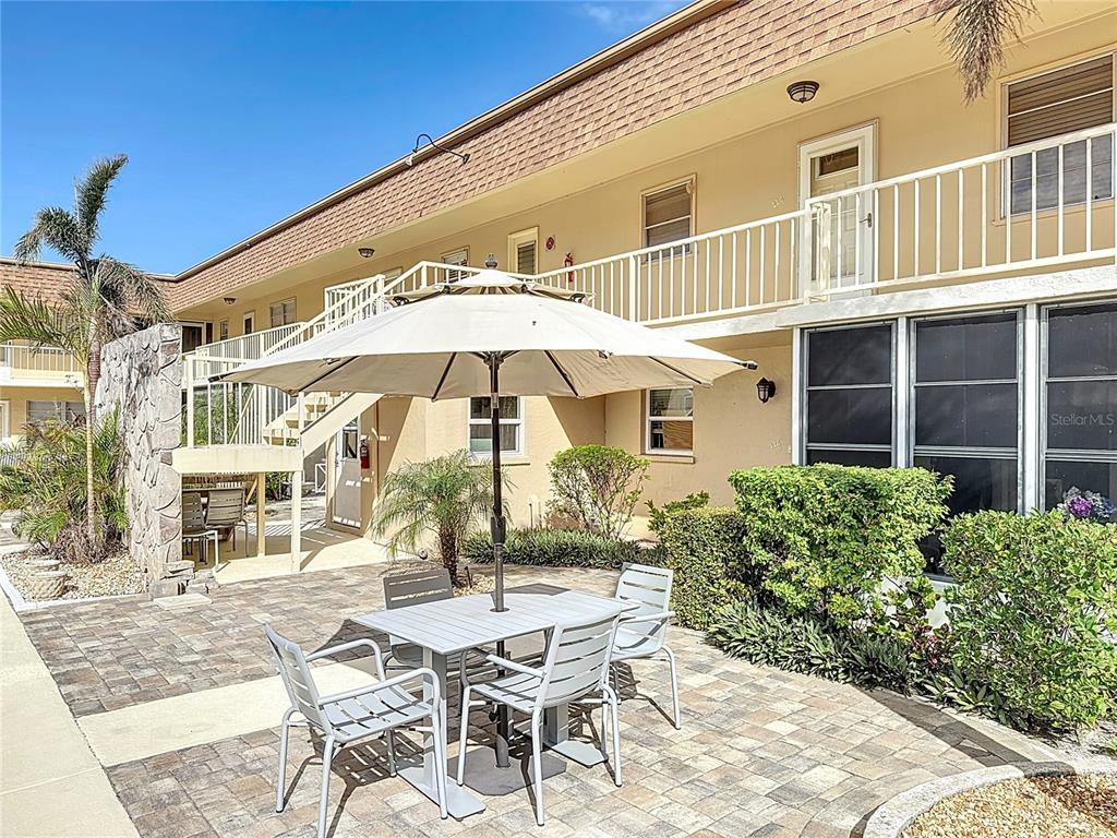 A patio with a table, chairs, and umbrella sits outside a two-story apartment building — 210 PARK BOULEVARD N UNIT 129, VENICE, FL