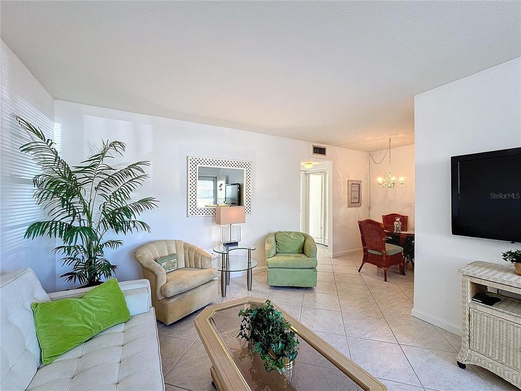 A living room and dining area feature light tile flooring, white walls, and wicker furniture — 210 PARK BOULEVARD N UNIT 129, VENICE, FL
