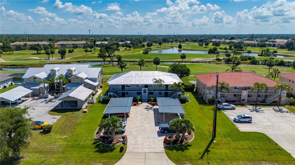An aerial view shows three apartment buildings with parking areas and a golf course behind — 1356 RIO DE JANEIRO AVENUE UNIT 108, PUNTA GORDA, FL