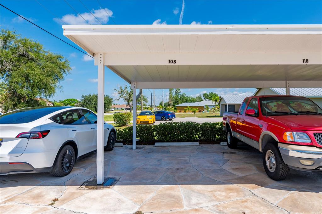 A covered carport with two parking spaces features a stone floor and numbered overhead signs — 1356 RIO DE JANEIRO AVENUE UNIT 108, PUNTA GORDA, FL