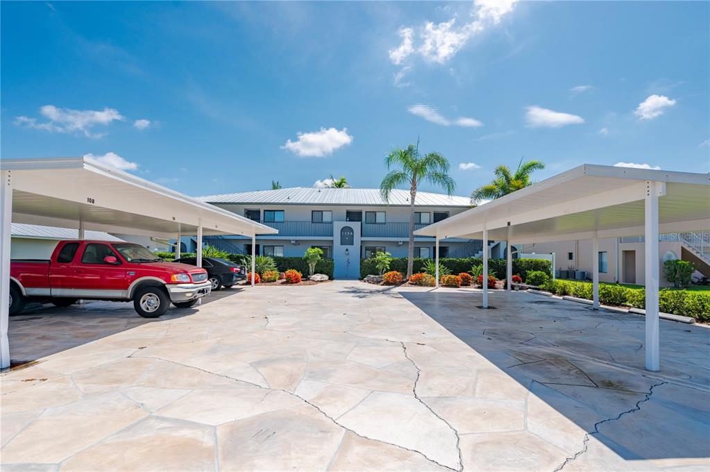 A two-story apartment building features covered parking spaces in a paved lot — 1356 RIO DE JANEIRO AVENUE UNIT 108, PUNTA GORDA, FL