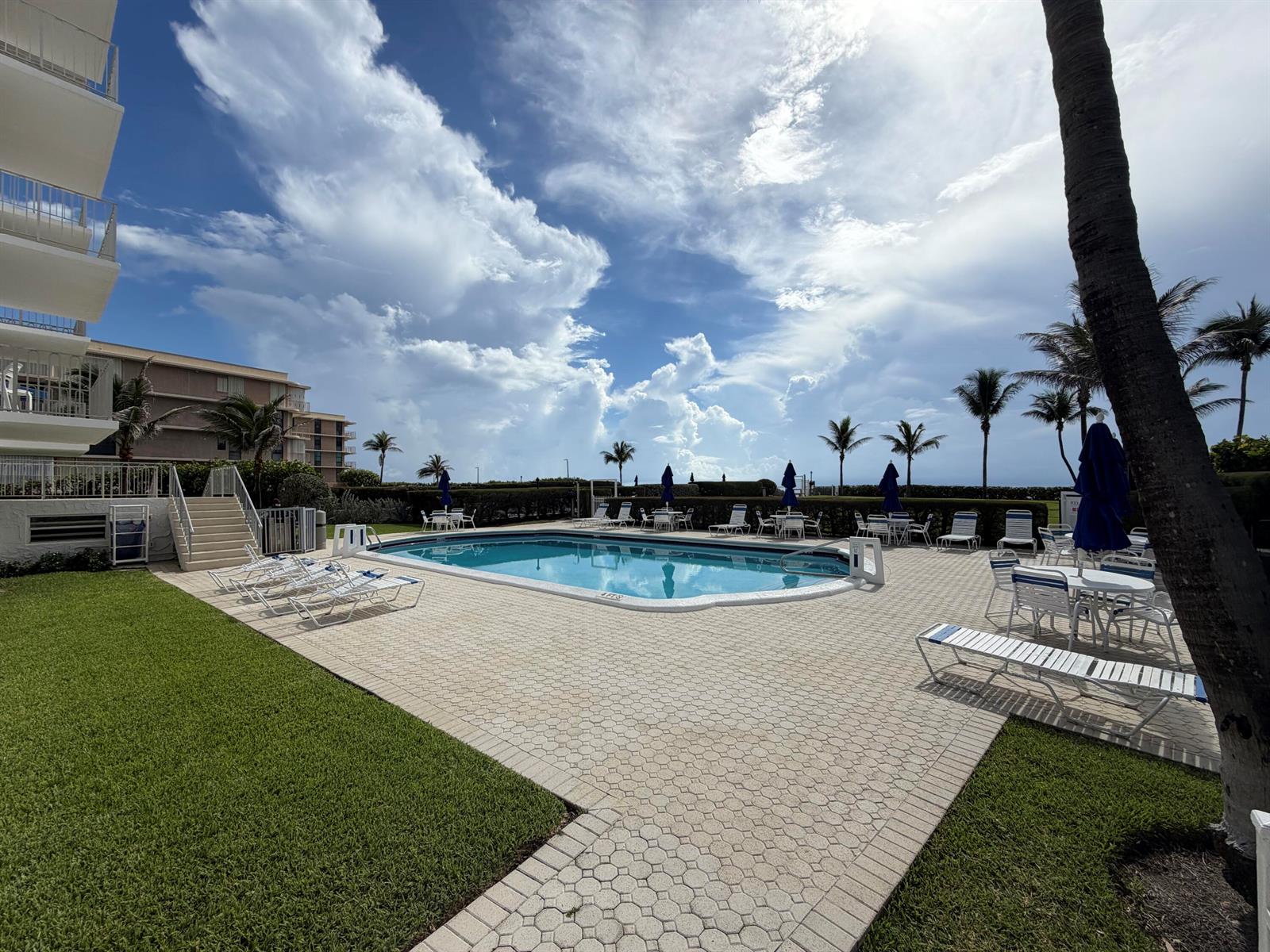 A swimming pool with lounge chairs and patio tables sits beside a multi-story apartment building — 3230 S Ocean Boulevard # C205, Palm Beach FL 33480, PALM BEACH, FL