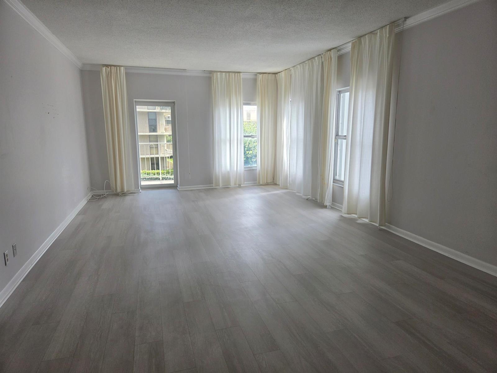 An empty living room features light gray wood-look flooring, white walls, and floor-to-ceiling curtains — 3230 S Ocean Boulevard # C205, Palm Beach FL 33480, PALM BEACH, FL