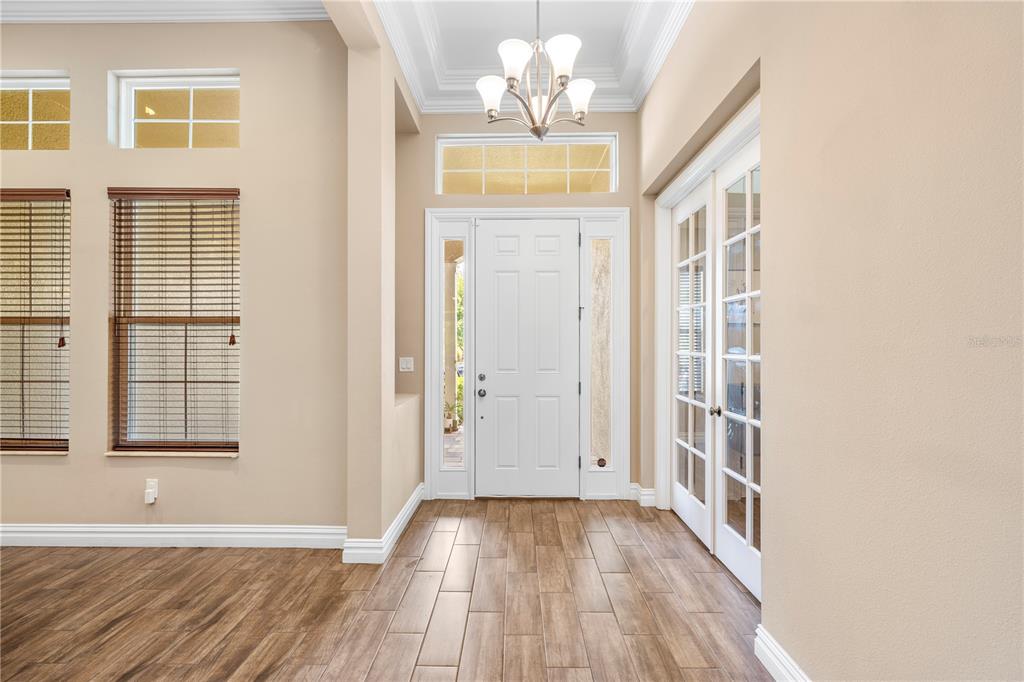 An entryway features wood-look tile flooring, a white front door with sidelights, and a chandelier — 16726 COURTYARD LOOP, LAND O LAKES, FL