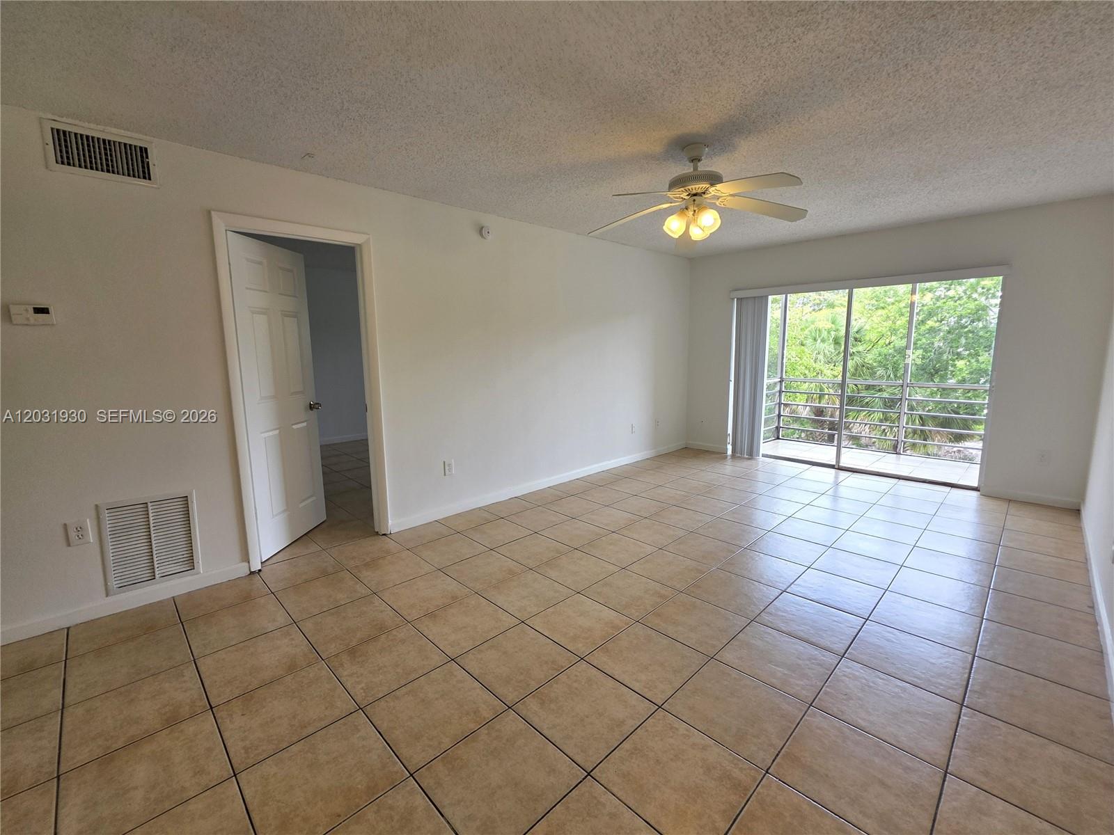 An empty room features beige tile flooring, a ceiling fan, and a sliding glass door — 2800 NW 56th Ave # E303, Lauderhill FL 33313, LAUDERHILL, FL