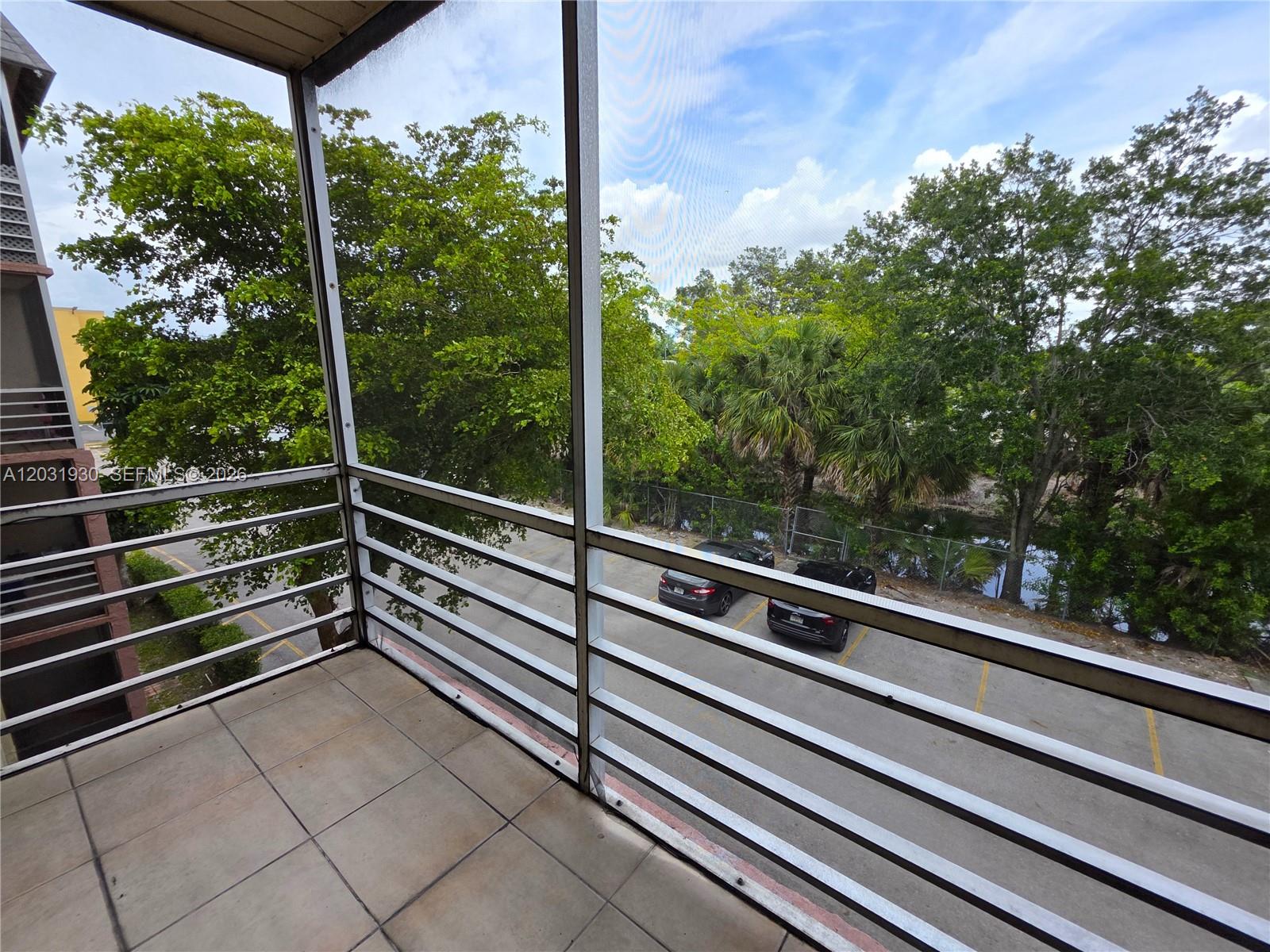 A screened-in balcony with tiled flooring overlooks a parking lot and trees — 2800 NW 56th Ave # E303, Lauderhill FL 33313, LAUDERHILL, FL