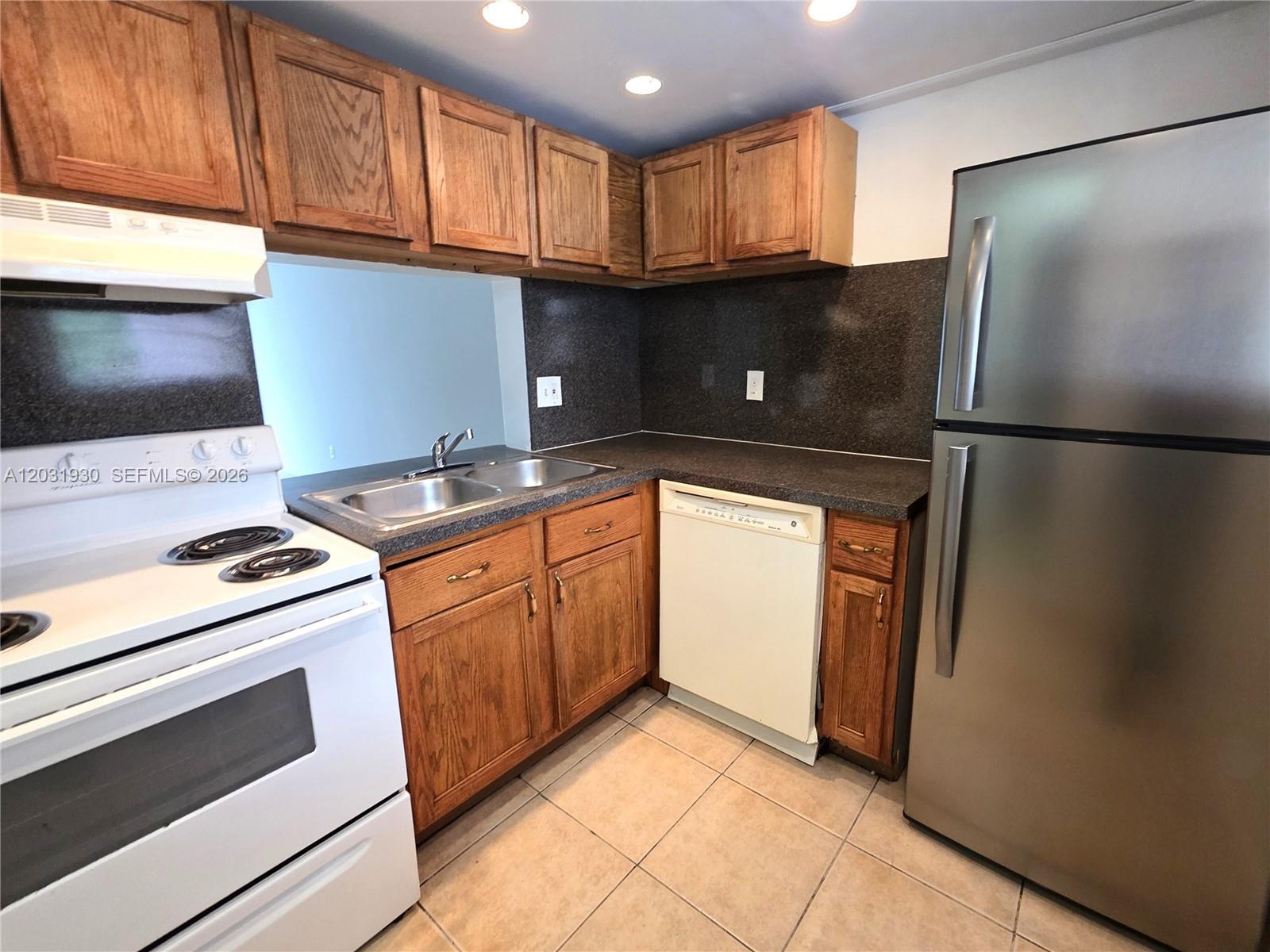 A kitchen features wooden cabinets, a white stove, a dishwasher, and dark countertops — 2800 NW 56th Ave # E303, Lauderhill FL 33313, LAUDERHILL, FL